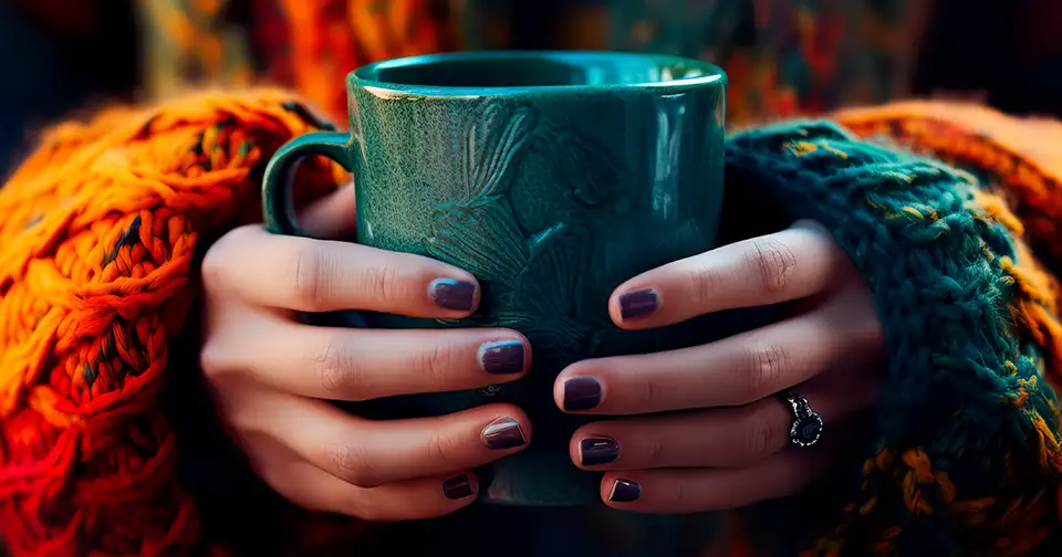 Woman holds a cup of steaming coffee, wrapped in a comfy sweater.