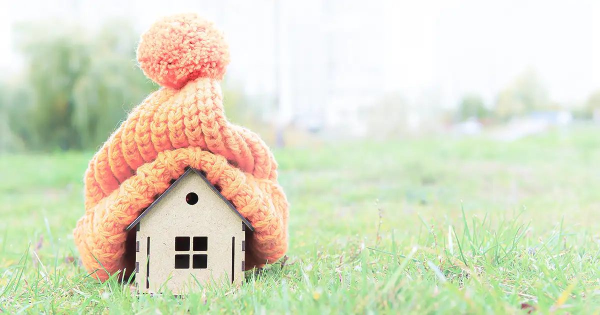 A tiny little model house with a crocheted cap over it.