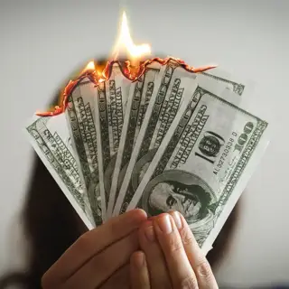 A woman holding a handful of $100 bills that are on fire.