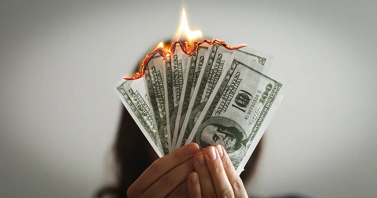 A woman holding a handful of $100 bills that are on fire.