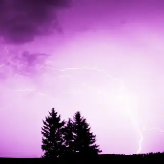 Lightning strikes the ground in the distance during an intense thunderstorm.