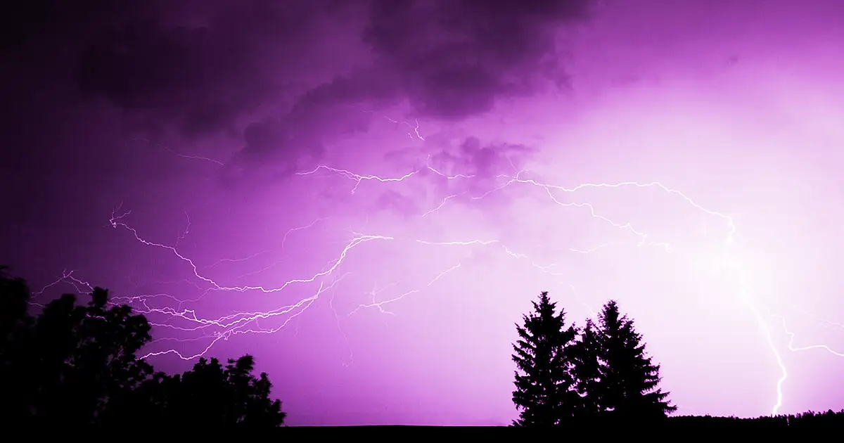 Lightning strikes the ground in the distance during an intense thunderstorm.