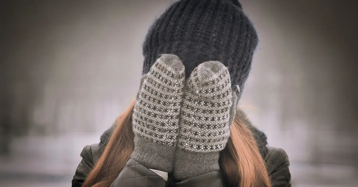 A woman, outside in the cold of winter, bundled up with a hat and mittens.