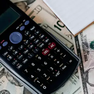 A calculator on top of a stack of one and five dollar bills.
