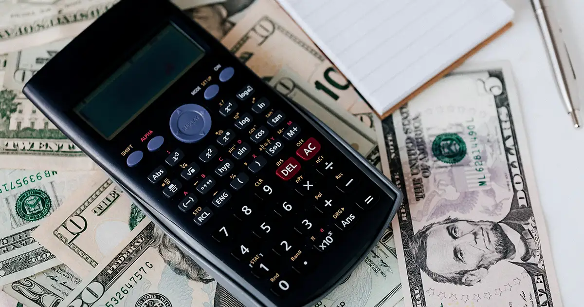 A calculator on top of a stack of one and five dollar bills.