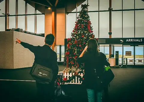 A couple in the airport, a big Christmas tree decorating the lobby.